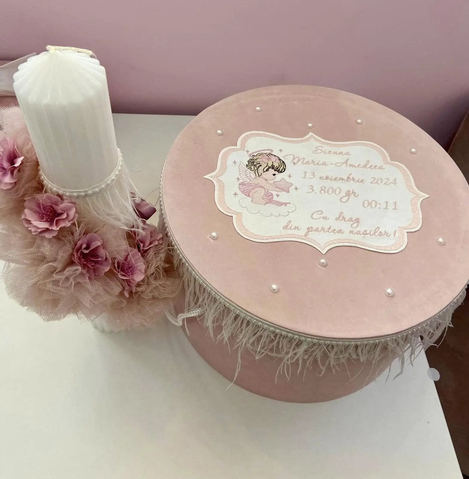 Cutie de trusou din catifea roz cu capac personalizat, lângă o lumânare decorată cu flori și pene