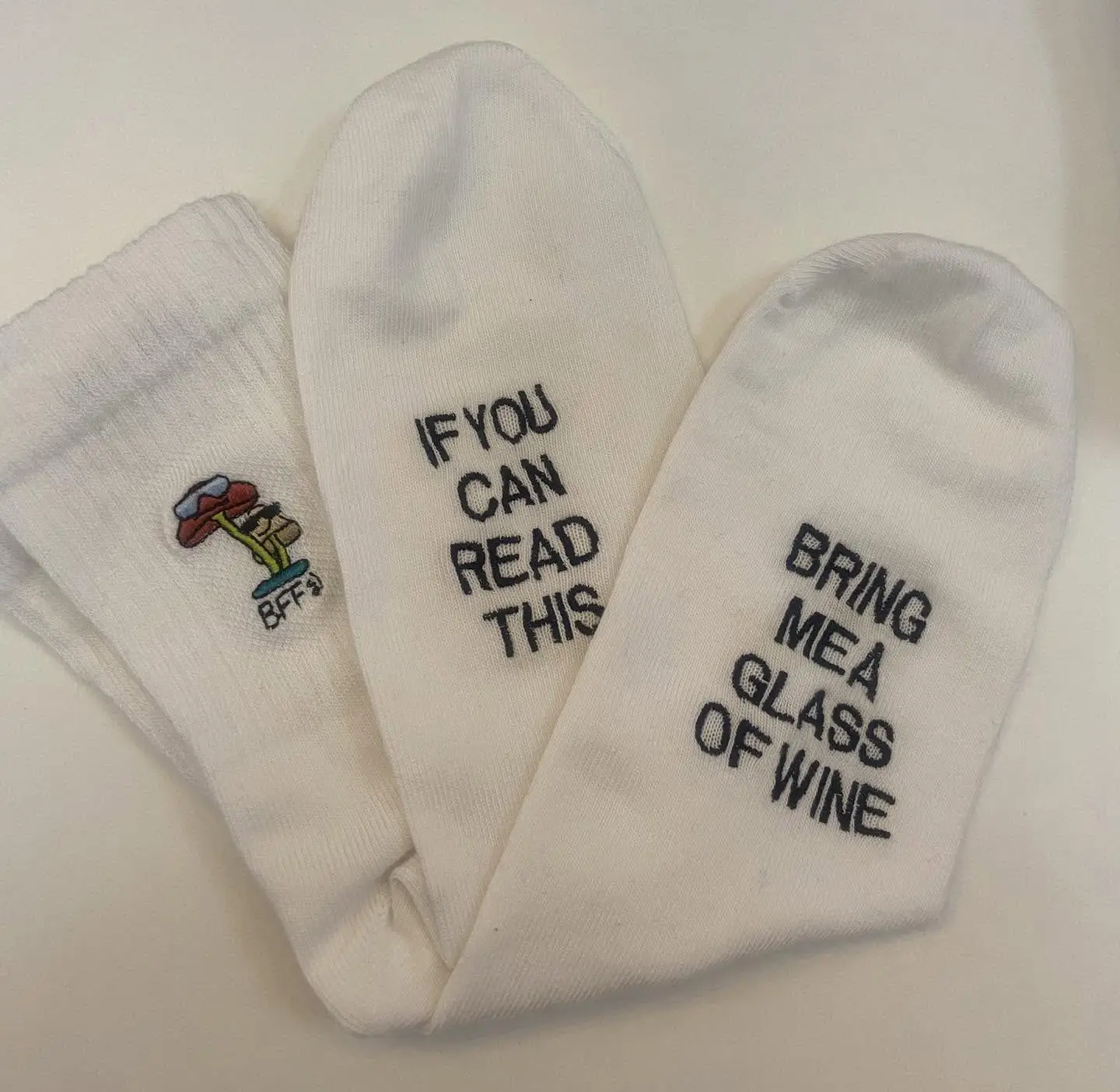 Șosete albe brodate cu mesajul „If you can read this, bring me a glass of wine” și o mașinuță